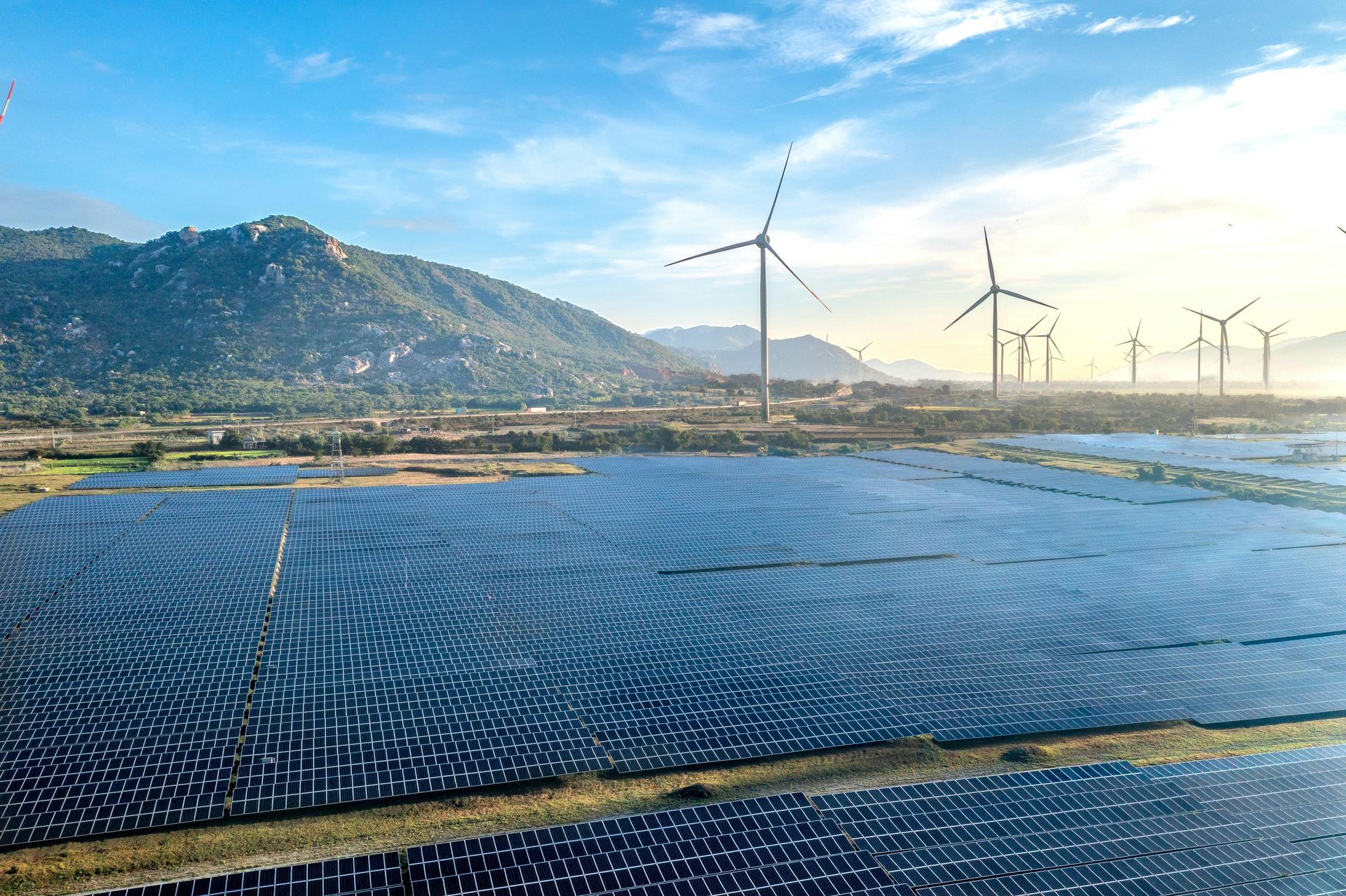 Solar array and wind turbines in a mountain landscape at sunrise